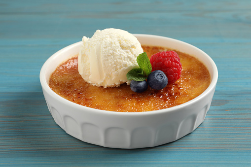 Delicious creme brulee with scoop of ice cream, fresh berries and mint on light blue wooden table, closeup