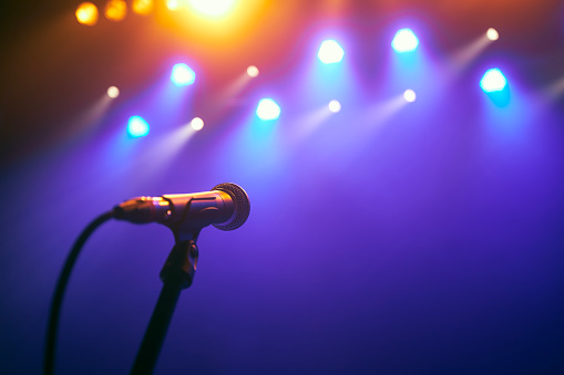 Selective focus on lluminated microphone on stage against colorful spotlights.