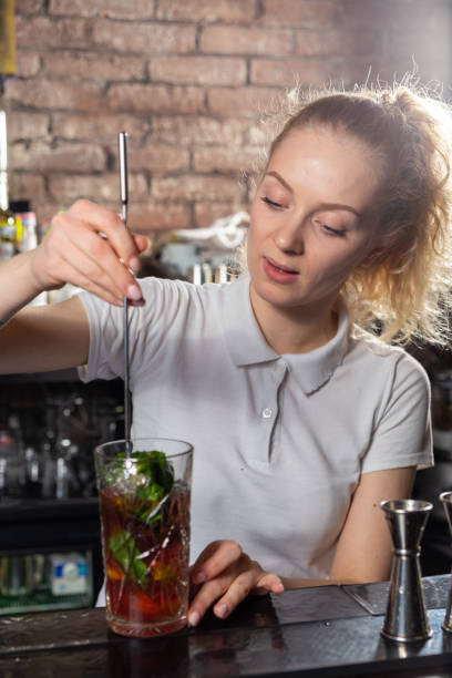 istock Young beautiful female bartender mixing a cocktail in a high glass. 1445405461