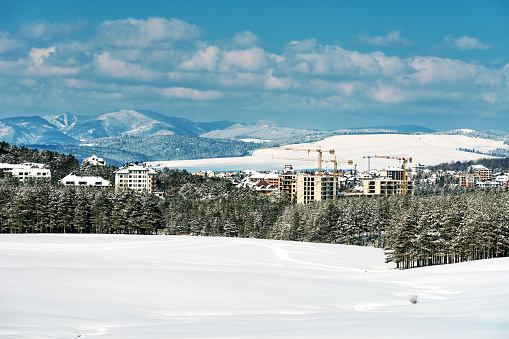 Construction industry apartment and housing development at Zlatibor in winter season under snow, buildings and cranes taking over the pine forest landscape