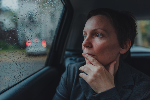 Worried businesswoman waiting in the car and looking out the window during rain, selective focus