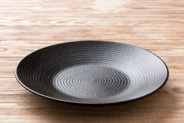 istock Perspective view of empty black plate on wooden background. Empty space for your design 1445408249