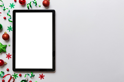 Christmas online shopping from home tablet pc with blank white display top view. Tablet with copy space on colored background with Christmas decorations balls,. Winter holidays sales background.