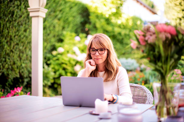 istock Middle aged woman using laptop while sitting on balcony at home 1445410188