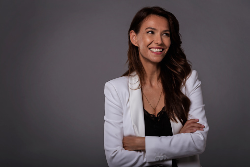 Studio portrait shot of attractive middle aged woman with toothy smile wearing blazer while standing at isolated dark background. Copy space.