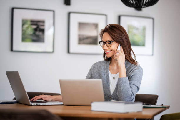 istock Business woman using mobile phone in front of laptops while working from home 1445410225