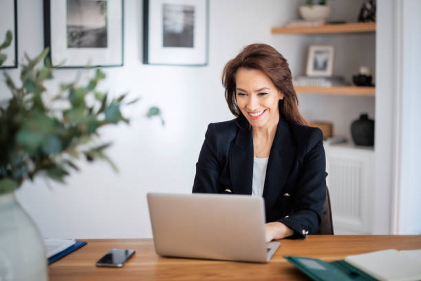 istock Happy middle aged woman sitting at tablet and using laptop while working at home 1445410227