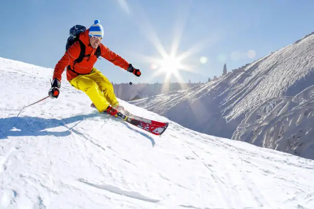 Photo of Skier skiing downhill in high mountains against blue sky.