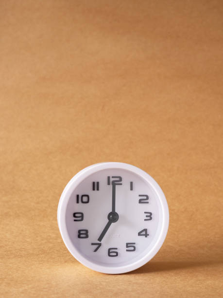 istock Vertical close up, white clock shows time at 7 o'clock on the office brown workplace tabletop. 1445412422