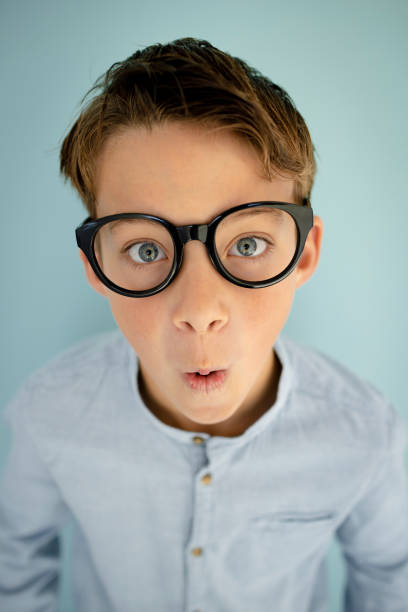 young cool boy with blue shirt, with big massive black glasses standing in front of blue background