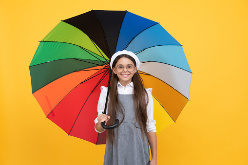 rainy weather forecast. back to school. tween with vivid rain protection. happy school girl in glasses. cheerful teen child under colorful parasol. kid in beret with rainbow umbrella. autumn season.