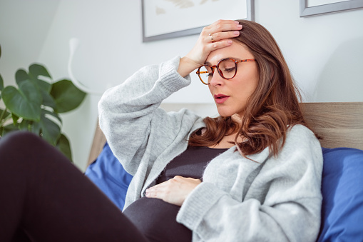 Pregnant woman lying on the bed and suffering headache ache, touching her belly.