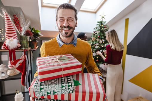 Time for celebration. Overjoyed arab man in santa hat holding stack of gift boxes and smiling at camera, posing over blue background, free space