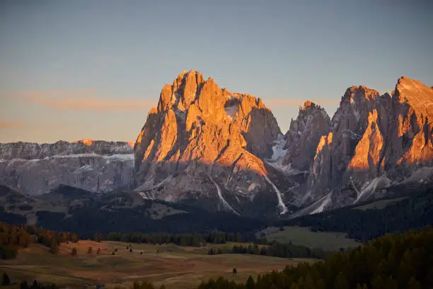 European Alps Langkofel mountain group in Dolomites. The sun has just set, the sky is blue. The sunlight is shining on the mountaintops.