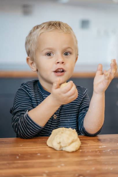 istock Young boy leaning on the kitchen counter and kneading cookie dough 1445416586