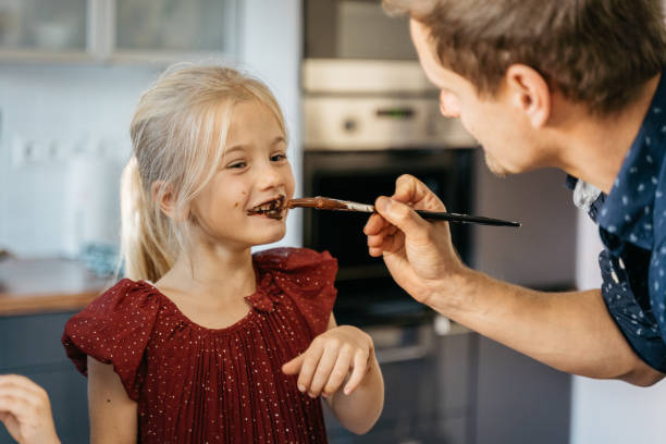 istock Father painting his daughter's lips and teeth with chocolate while preparing cookies 1445419764