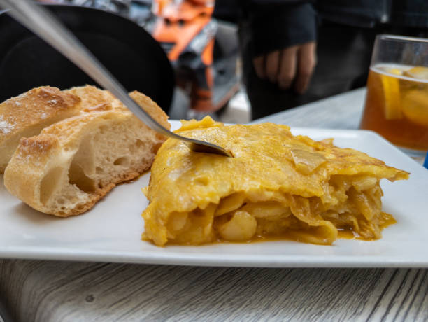 Tasty potato omelette with its slightly curdled egg, two pieces of bread to accompany it and a fork stuck in the omelette, typical Spanish tapa appetizing potato tortilla tapa, typical spanish dish spanish breakfast stock pictures, royalty-free photos & images