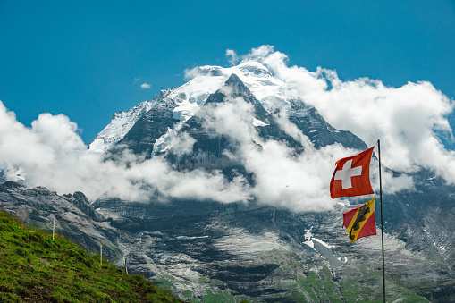 The summit of Mount Jungfrau in the Bernese Alp, Switzerland. The summit is partly in the clouds. In the foreground the flags of Canton Bern and Switzerland.