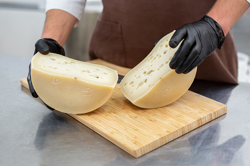 Cheese maker cuts a cheese head with a knife on a wooden board at a private cheese factory