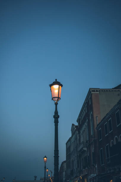 Light trail illuminating a canal in venice at night, with a tall brick tower standing on the right and traditional venetian buildings lining the canal