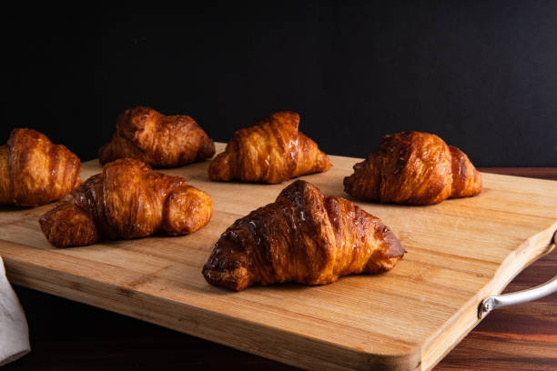 Golden brown croissants on a cutting board with black background, front view stock photo