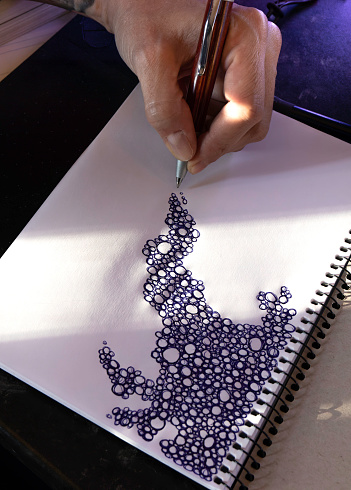 Close up of a hand drawing a pattern of scribbled bubbles on a blank scrapbook. Boredom, creativity concept
