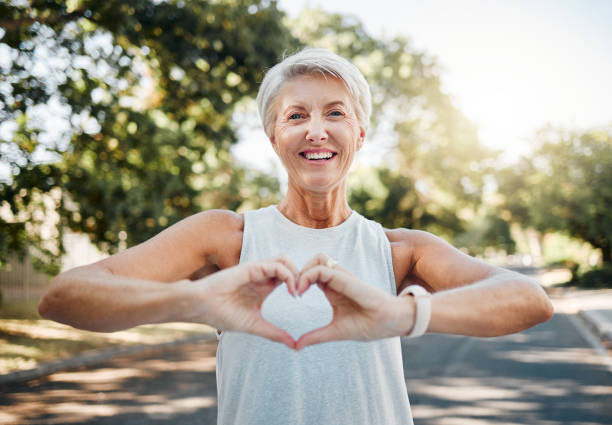 fitness, glückliche und herzhände der alten frau in der natur nach dem laufen für gesundheit, wellness und training. lächeln, motivation und ruhe mit senior dame und zeichen für liebe, glauben und training in der natur - healthy man stock-fotos und bilder