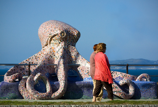 A Coruña, Galicia, Spain- May 16, 2010: Rear view of two middle aged women walking together passing by Octopus  sculpture in a sea waterfront promenade, Javier M. Padín Martínez  sculptor.  A Coruña city, Galicia, Spain.