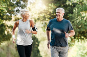 Health, senior couple and running in nature or park for exercise, fitness and wellness. Retirement, elderly man and woman enjoy walk, fresh air and talk in forest for workout, training and relax.