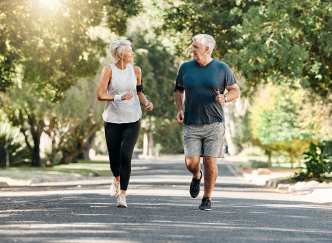 Health, senior couple and running while talk and exercise for fitness, wellness and healthy together in nature. Retirement, man and woman enjoy workout, chatting and jog outside in park on sunny day