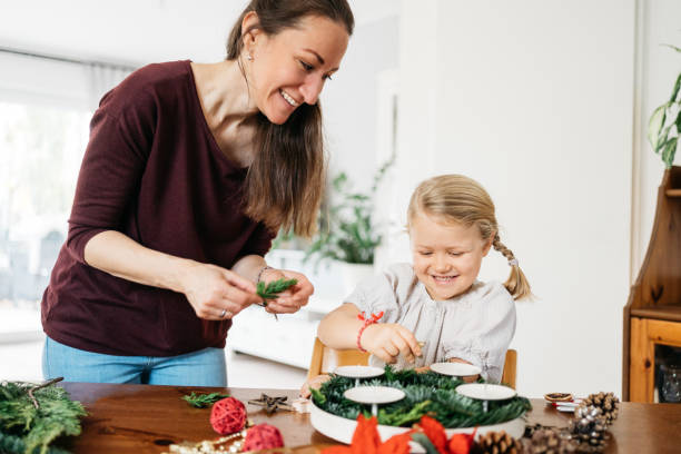 little girl and her mother making advent wreath with candles, pine cones and stars little girl and her mother making advent wreath with candles, pine cones and stars advent candle wreath adventskranz stock pictures, royalty-free photos & images