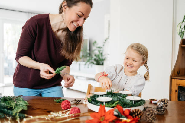 little girl and her mother making advent wreath with candles, pine cones and stars little girl and her mother making advent wreath with candles, pine cones and stars advent candle wreath adventskranz stock pictures, royalty-free photos & images