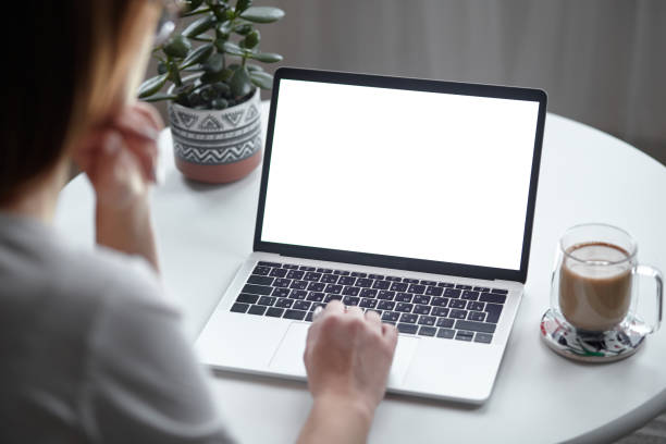 istock Mockup white screen laptop woman using computer while sitting at table at home, back view 1445441524