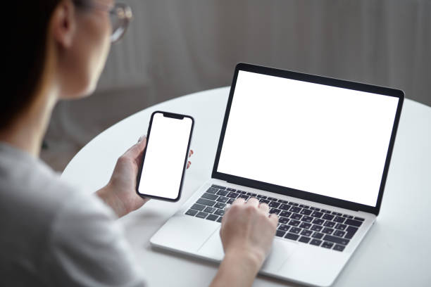 istock Mockup white screen laptop and mobile phone woman using computer while sitting at table at home, back view 1445441558