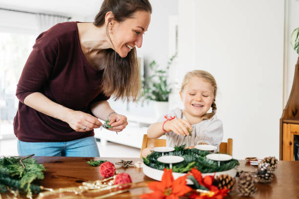 little girl and her mother making advent wreath with candles, pine cones and stars little girl and her mother making advent wreath with candles, pine cones and stars advent candle wreath adventskranz stock pictures, royalty-free photos & images