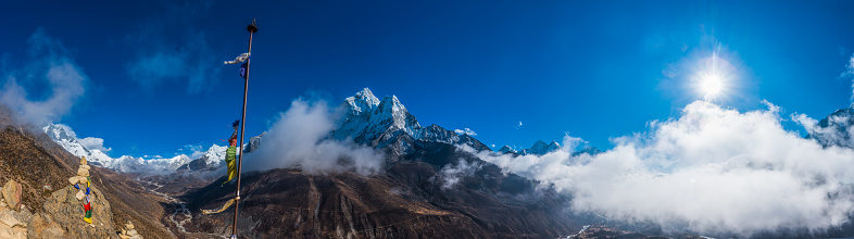 Bright sun in the deep blue high altitude skies above the clouds swirling through the snow capped peaks of the Himalayan mountains, from Ama Dablam to Makalu and Lhotse, Nepal.