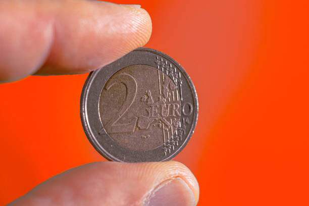 istock 2 euro coin face held between thumb and index finger.red background. 1445456780