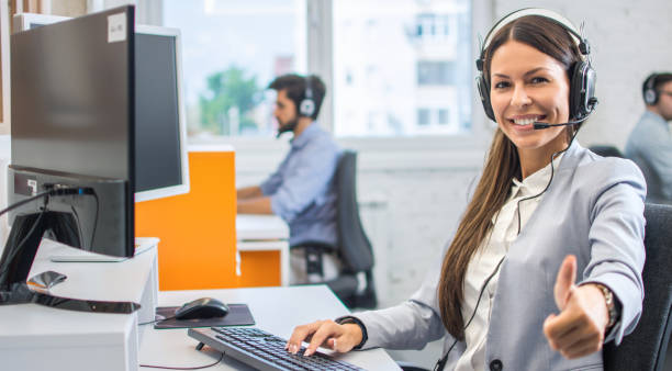 verticale de la belle jeune femme utilisant le casque affichant des pouces vers le haut du geste. femme d'agent de service de service de client travaillant dans le centre d'appel et affichant le signe de succès avec une main. - dispatcheur photos et images de collection