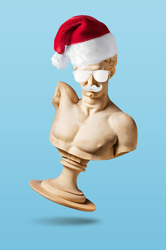 Creative layout with old statue in Santa hat on light blue background. Minimal Christmas or New Year concept.