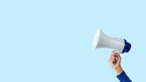 Megaphone in woman hand on blue background. Creative announcement concept.