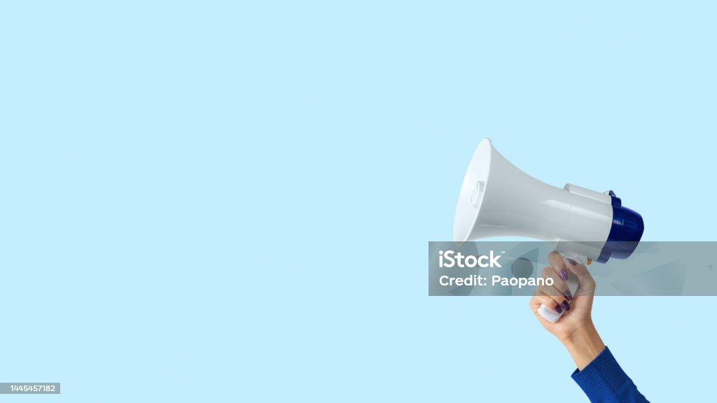 Megaphone in woman hand on blue background. Creative announcement concept. Megaphone Stock Photo