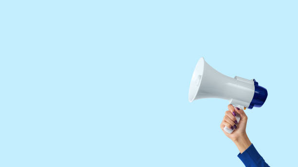 Megaphone in woman hand on blue background. Creative announcement concept. Megaphone in woman hand on blue background. Creative announcement concept. public address system stock pictures, royalty-free photos & images