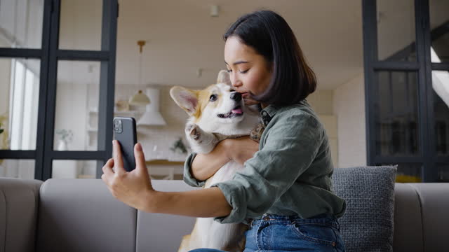 Young Asian woman takes selfie with cute dog sitting on sofa