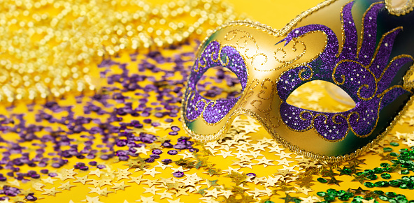 Mardi Gras Luxury Masquerade venetian festival carnival mask, gold color beads and golden, green, purple confetti on yellow background. Party invitation, greeting card, winter carnival celebration concept.