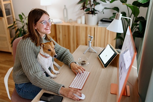 Woman sitting with her dog at the desk using desktop computer for online shopping
