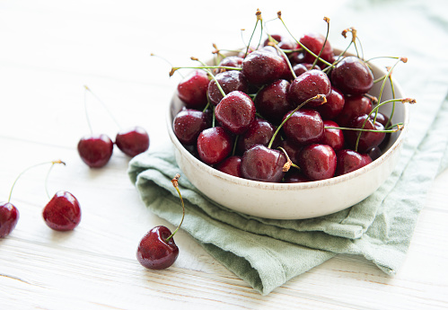 Fresh red cherries fruit in bowl on a white wooden background