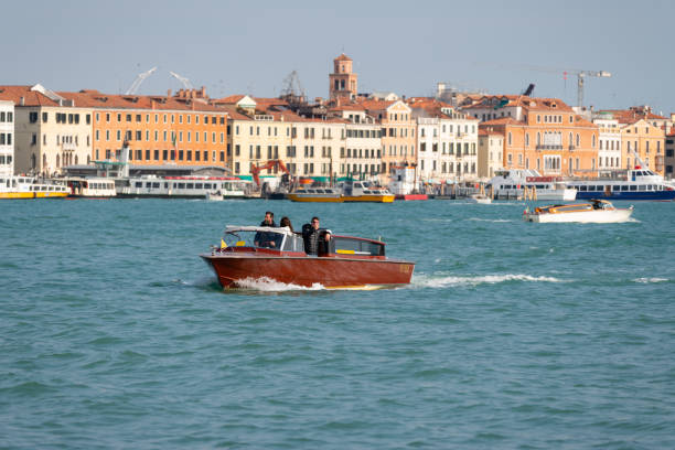 Travel In Venice A traditional wooden-hulled speedboat traverses the waters of the Grand Canal in Venice. watertaxi stock pictures, royalty-free photos & images