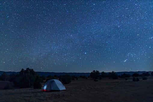 A tent under a star-filled night sky in the Grand Staircase-Escalante National Monument, a few miles south of the town of Escalante, Utah. Fiftymile Mountain is seen in the distance.