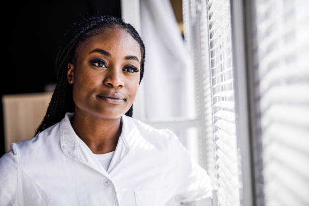 istock Smiling female scientist standing by the window, looking outside, pondering during a work break 1445473257