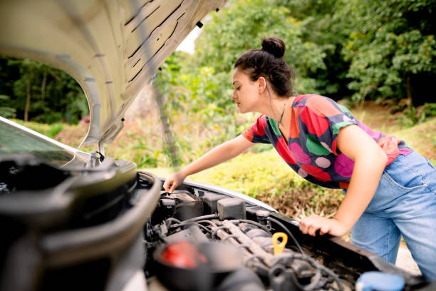 mujer joven revisando la conexión de la batería de su automóvil - car stranded women breakdown fotografías e imágenes de stock